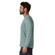 En mand med brunt hår og skæg ses i profil, iført en Patagonia Long-Sleeved Capilene Cool Shirt for men i Blue Sage - Light Blue Sage X-Dye, sammen med mørke bukser, stående mod en hvid baggrund.