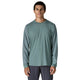 En mand med kort, krøllet hår og et neutralt udtryk står og kigger fremad i en Patagonia Long-Sleeved Dirt Craft Jersey, Herre, Blue Sage, sammen med mørke bukser mod en almindelig hvid baggrund og viser trailrunning-stil.