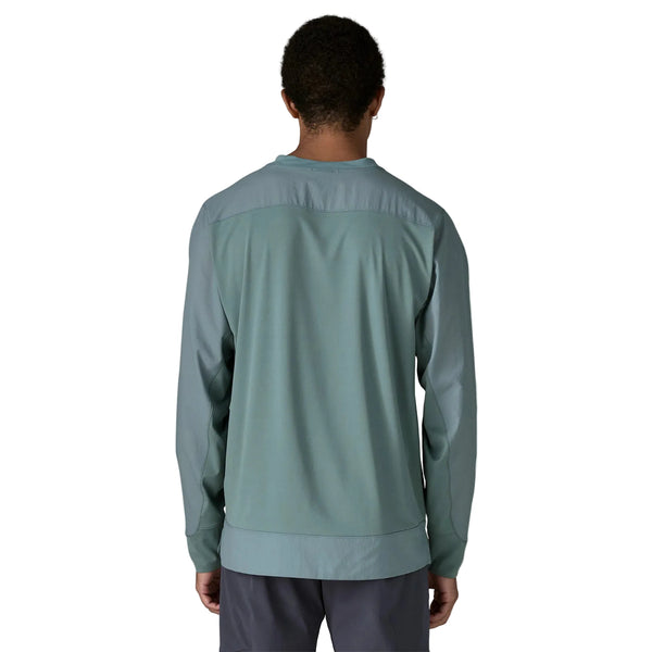 En person med kort hår ses bagfra iført en Patagonia Long-Sleeved Dirt Craft Jersey, Herre, Blue Sage og mørke bukser på en ensfarvet hvid baggrund - ideelt til trailløbseventyr.