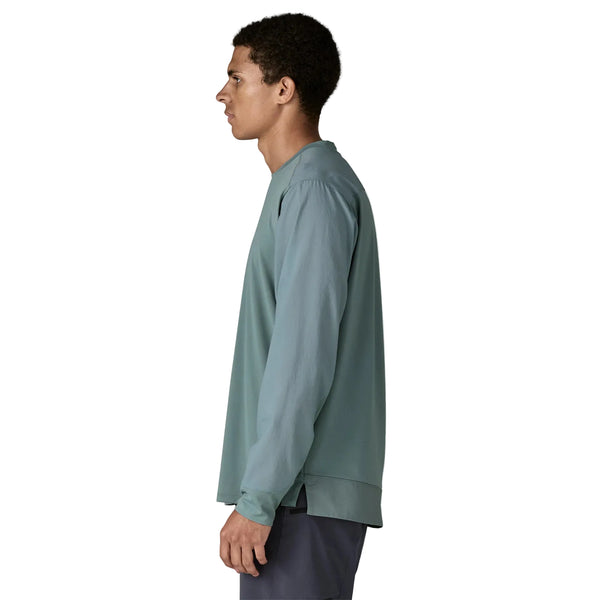 En person i profil vender mod venstre og er iført en løstsiddende, langærmet Patagonia Long-Sleeved Dirt Craft Jersey til mænd i Blue Sage og mørke shorts - perfekt til trailløb. Baggrunden er helt hvid.