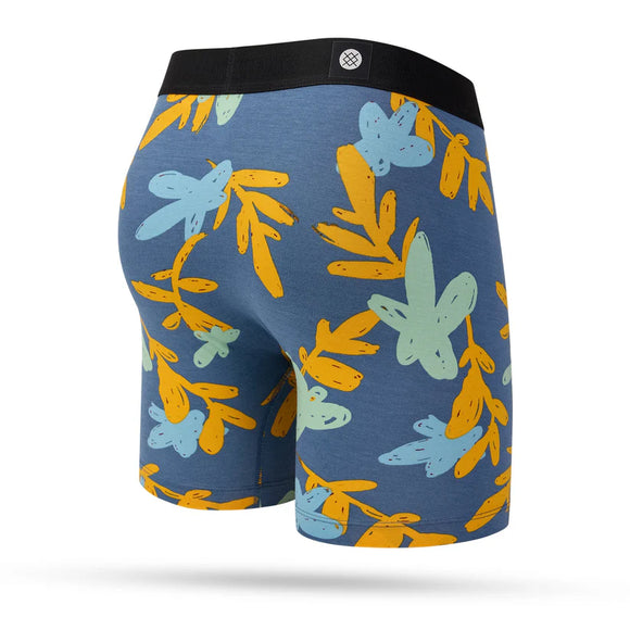Stance In Paradise Wholester boxershortsene her har et flerfarvet bladmønster med blå, gule og lyseblå toner plus en sort linning, der vises stilfuldt mod en hvid baggrund.