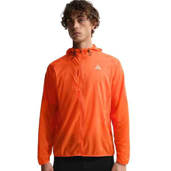En person iført Nike ACG Trail Aireez Jkt til mænd i Safety Orange/Summit White med lynlås foran og et lille logo på brystet står på en almindelig hvid baggrund.