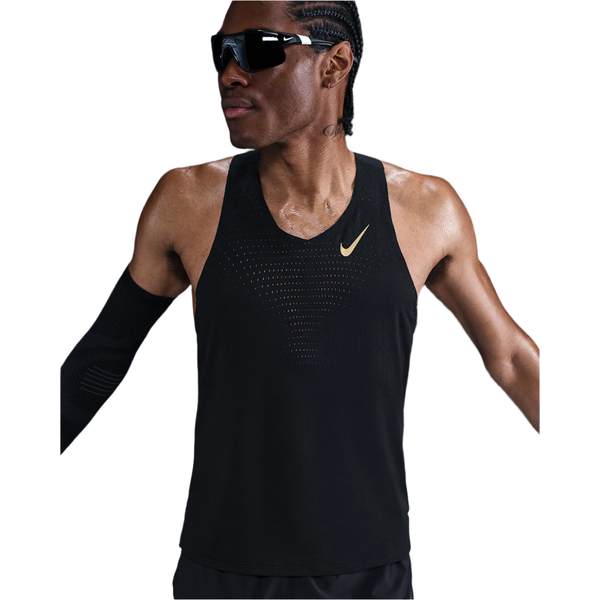 En person iført sorte solbriller, en Nike M Nk Dfadv Aeroswift Jakob Singlet til mænd i Black/Metallic Gold, et sort ærme og sorte shorts står med let udstrakte arme mod en hvid baggrund.