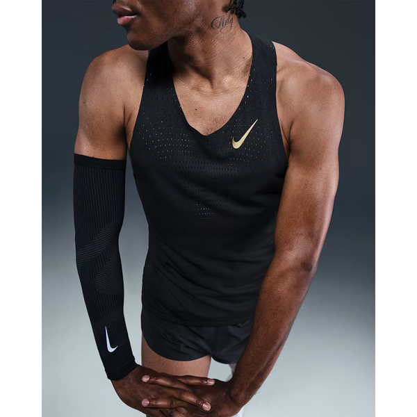 En person iført en sort Nike M Nk Dfadv Aeroswift Jakob Singlet (Black/Metallic Gold) står med armene over kors, parret med et sort Nike-ærme på venstre arm. Vedkommende har en tatovering i nakken og står på en almindelig, mørk baggrund.