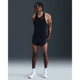 En person iført Nike M Nk Dfadv Aeroswift Jakob Singlet, Herre, Black/Metallic Gold med sorte løbeshorts, hvide sneakers og solbriller står med armene bag ryggen mod en mørk baggrund.