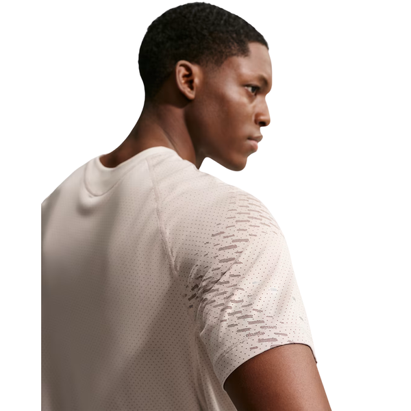 En mand med kort hår ses bagfra og fra siden iført en lys beige Nike Stride Novelty SS Running Top, Herre, Cream Ii/Mink Brown/Reflective Silv med perforeret åndbart design og diskret mønstrede ærmer mod en hvid baggrund.
