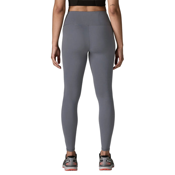 En person ses bagfra iført Patagonia Mas Maipo Tights, Dame, Smolder Blue, en sort crop top og grå sportssko med orange såler på en hvid baggrund.