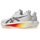 Et par hvide Asics Megablast-løbesko i farvekombinationen Unisex White/Orange Glow, med sorte Asics-logoer og orange-gule detaljer i farveovergang på mellemsålerne. Disse sko, der bærer navnet Megablast, er udstyret med det innovative FF TURBO SQUARED-skum, der sikrer maksimal affjedring, og har et elegant design med lysebrune ydersåler.