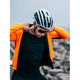En cyklist iført hvid og sort hjelm og solbriller justerer en lys orange jakke over Fusion Merino 150 LS, Herre, Black-trøjen på en klippefyldt udendørs baggrund.