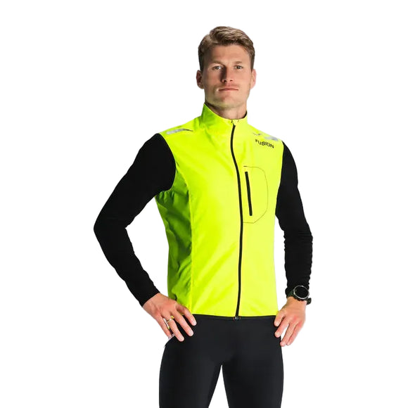 En person vender sig mod kameraet iført Fusion S1 Run Vest, Herre, Yellow over en sort langærmet skjorte og sorte bukser. Vesten har en høj krave og en synlig brystlomme. Baggrunden er almindelig lysegrå.