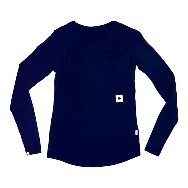 Saysky W Merino Base 165 Long Sleeve, Dame, Blue ligger fladt med ryggen opad og har et lille hvidt rektangulært mærke med en sort stjerne nederst i højre side og et lille hvidt mærke i bunden.