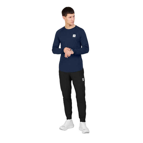 En mand iført en marineblå SAYSKY Merino Base 165 langærmet trøje, sorte joggingbukser og hvide sneakers.