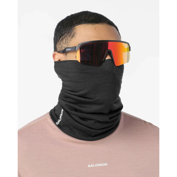 En person, der bærer en Deep Black Salomon Merino-halsvarmer og orangefarvede sportsolbriller til udendørsaktiviteter.