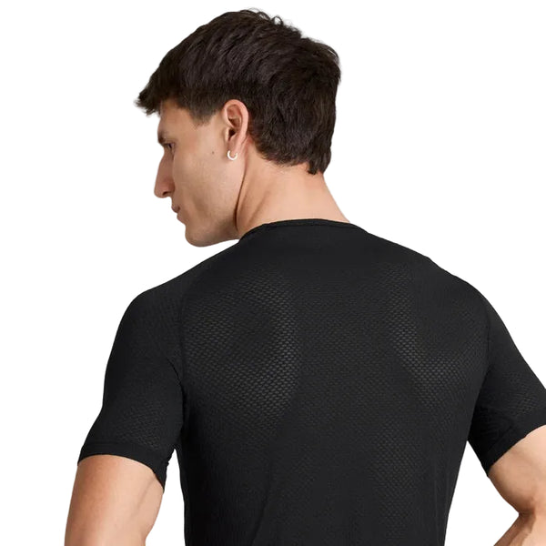 Der ses en person med kort, brunt hår set bagfra, iført en tætsiddende sort Saysky Mesh Base Layer T-shirt i unisex-udgave med struktureret overflade. Personens venstre arm er let bøjet, og hovedet er vendt mod venstre.