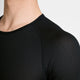Et nærbillede af en person, der bærer Saysky Mesh Base Layer-T-shirten i sort, med et struktureret bikagemønster og et åndbart mesh-design. Kun halsen, skuldrene og den øverste del af brystet er synlige på en ensfarvet lys baggrund.