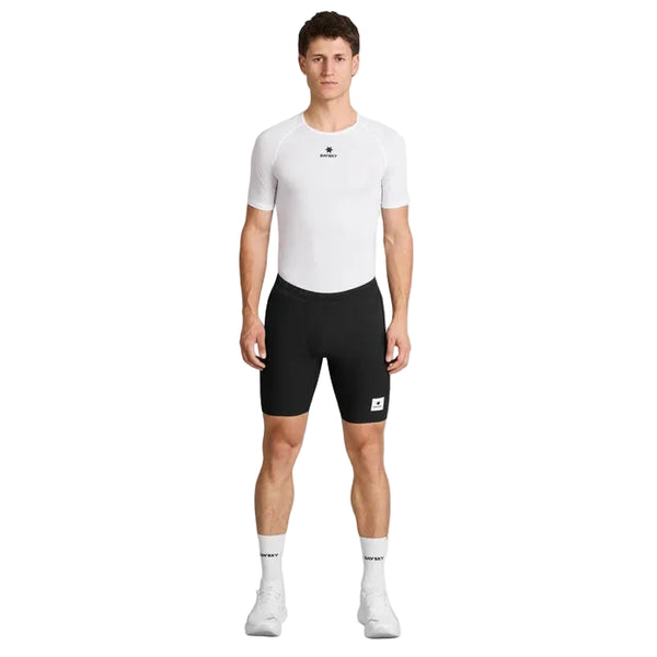 En person står med ansigtet vendt fremad foran en ensfarvet hvid baggrund og har en hvid Saysky Mesh Base Layer T-shirt på, kombineret med sorte cykelshorts, hvide sokker og hvide sportssko.