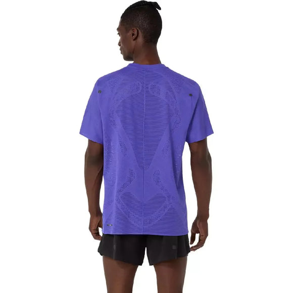 En person med mørk hud og en lille topknude ses bagfra iført en ASICS Metarun Ss Top, Herre, Cobalt Burst med ACTIBREEZE-teknologi og et struktureret, ventileret mønster, parret med sorte shorts.