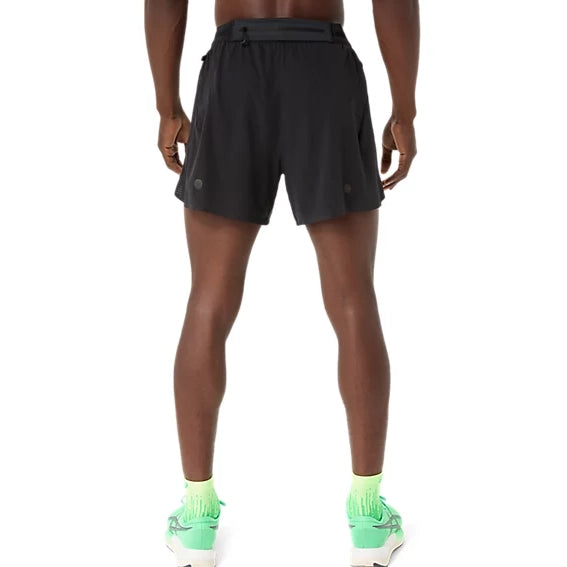En person står med ryggen til kameraet og har ASICS Metarun 5In Shorts, Herre, Performance Black på – stilfulde løbeshorts til mænd – kombineret med lysegrønne sokker og lysegrønne løbesko. Baggrunden er helt hvid.
