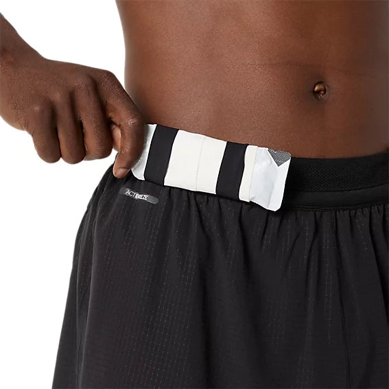 En person stikker en stribet lomme med påskriften »ACTIVIZE« ind i linningen på sine Asics Metarun 5In Shorts, Herre, i farven Performance Black. Kun overkroppen og hånden er synlige, hvilket fremhæver det praktiske design af disse performance-shorts.