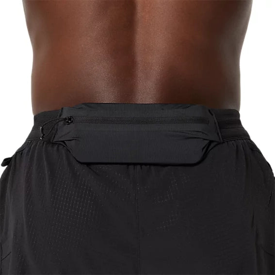 Nærbillede af en persons lænd, hvor personen bærer Asics Metarun 5In Shorts, Herre, Performance Black, sammen med et sort løbebælte eller en løbetaske med lynlås. Baggrunden er ensfarvet, og fokus er på tasken.