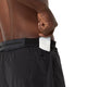 Man ser en person, der bærer ASICS Metarun 5In Shorts, Herre i farven Performance Black, sætte en hvid, rektangulær genstand – muligvis en telefon – ned i sidelommen med lynlås. Billedet viser et nærbillede af personens overkrop og hånd på en ensfarvet hvid baggrund.