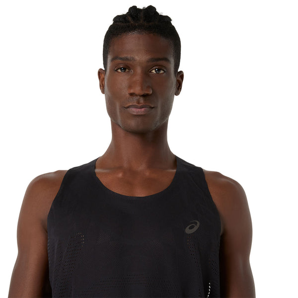 En person med kort flettet hår er iført Asics Metarun Singlet, Herre i Performance Black, en populær løbetøj herre, og kigger direkte ind i kameraet mod en almindelig hvid baggrund.