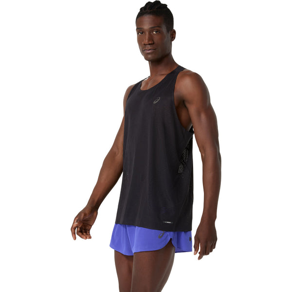 En mand i en Performance Black ASICS Metarun Singlet og blå løbeshorts står med ansigtet fremad og den ene arm afslappet langs siden, mens han kigger lidt til venstre. Ideelt løbetøj herre for både komfort og stil.