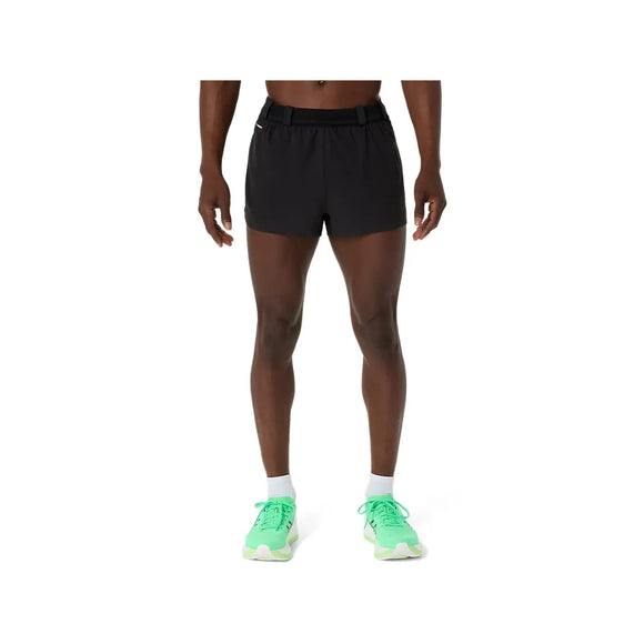 En person står med ansigtet fremad og er iført ASICS Metarun Split Short, Herre, Performance Black, et bælte, hvide sokker og lysegrønne løbesko. Billedet viser personen fra bryst til fødder.