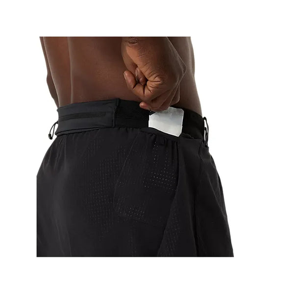 En person stikker en rektangulær genstand ned i baglommen på Asics Metarun Split Short, Herre, Performance Black. Kun overkroppen og hånden er synlige, hvilket understreger disse performance-shorts' funktionalitet mod en hvid baggrund.