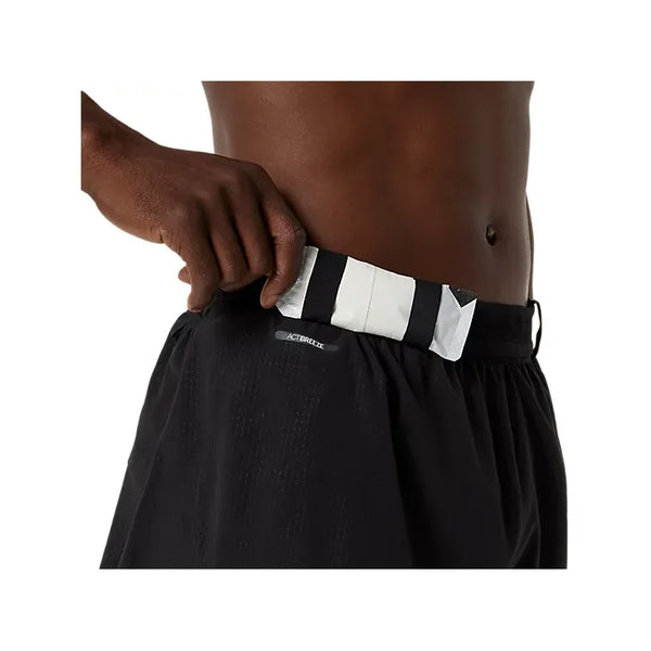 En person justerer linningen på Asics Metarun Split Short, Herre, Performance Black, og afslører det stribede inderbånd og et lille AEROREADY-mærke. Kun overkroppen og hånden er synlige, hvilket understreger disse alsidige løbeshorts.