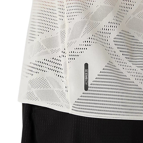 Nærbillede af Metarun Ss Top, Dame, Cream fra Asics – en hvid, perforeret løbetrøje med et lille rektangulært ACTIBREEZE-mærke tæt på nederkanten. Stoffet har et geometrisk mønster af små huller og ses her sammen med sorte bukser.