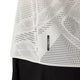 Nærbillede af Metarun Ss Top, Dame, Cream fra Asics – en hvid, perforeret løbetrøje med et lille rektangulært ACTIBREEZE-mærke tæt på nederkanten. Stoffet har et geometrisk mønster af små huller og ses her sammen med sorte bukser.