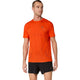 En person står foran en hvid baggrund iført en Metarun Ss Top til mænd i farven »cherry tomato« fra Asics og sorte shorts, mens vedkommende kigger lidt til siden.
