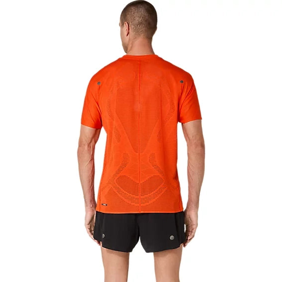 En mand står med ryggen til og er iført en orange Asics Metarun Ss Top, Herre, Cherry Tomato – en løbe-T-shirt til mænd med netlignende ACTIBREEZE-mønstre på ryggen – samt sorte løbeshorts, foran en ensfarvet hvid baggrund.