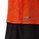 Nærbillede af en orange sportstrøje i netstof, Asics Metarun SS Top, Herre i farven Cherry Tomato, med geometriske ventilationshuller, båret over sorte shorts med et diskret gittermønster.