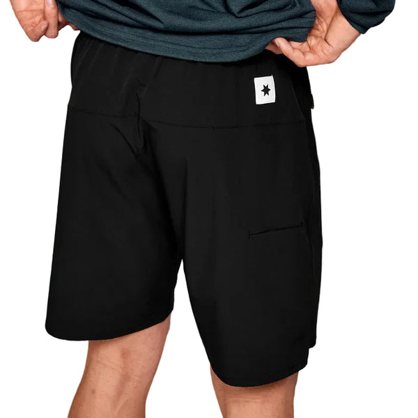 En mand iført Saysky Motion Running Shorts 8" i sort står med ryggen til og viser det hvide stjernemærke på den bageste linning og en lomme i højre side. Han bruger shortsene sammen med en mørk skjorte.