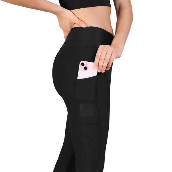 En person, der har Saysky Motion+ lange tights til kvinder i sort på, lægger en lyserød smartphone ned i en sidelomme. Personen har desuden en sort crop-top på, og kun overkroppen og benene er synlige på en hvid baggrund.