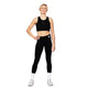 En kvinde står på en hvid baggrund iført en sort sports-BH, Saysky Motion+ lange tights, hvide sokker og hvide sportssko. Hun har den ene hånd på hoften, mens hun smiler.