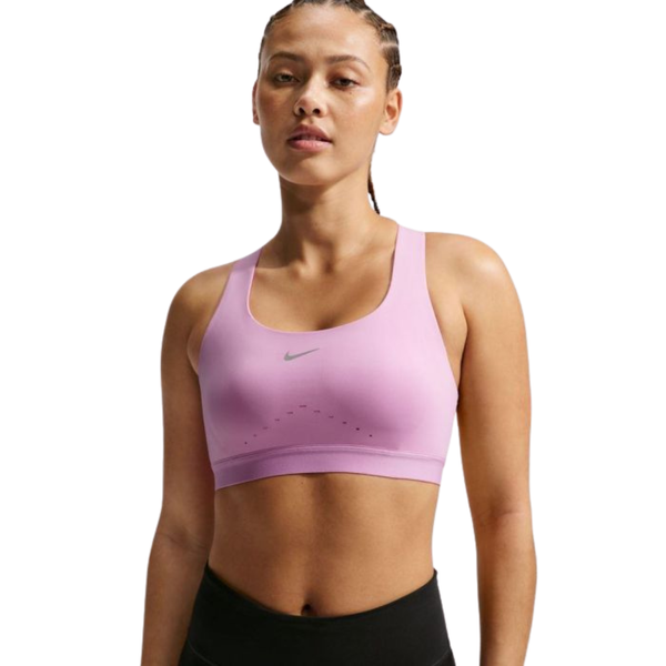 En kvinde med flettet hår bærer en Nike Nk Swift Hs BH til kvinder i Lt Magenta/Reflective Silver og sorte leggings, mens hun står og kigger ind i kameraet med et neutralt udtryk mod en hvid baggrund.