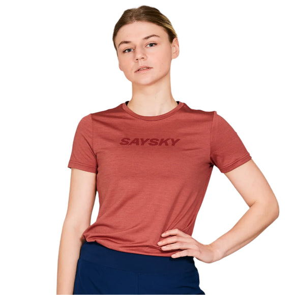 En kvinde står foran en hvid baggrund iført Saysky Logo Pace-T-shirten til kvinder i farven Red Melange med »SAYSKY« på forsiden og mørke bukser, med den ene hånd på hoften.