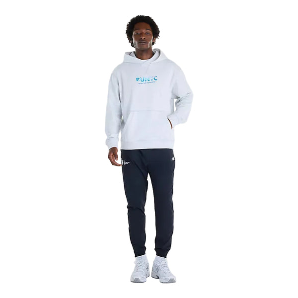 En person har en lysegrå New Balance NYC Marathon Athletics Graphic-hoodie (herre, farven Ash Heather) med et blåt motiv på brystet, mørke joggingbukser og lyse sportssko på.