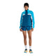En person iført en blå og hvid New Balance NYC Marathon-jakke, en Dame Streamsong-løbejakke med lynlås og matchende blå sportsshorts.