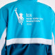 Bagside af en vind- og vandafvisende New Balance NYC Marathon-jakke, dame, i farven Streamsong, med Frihedsgudinden som motiv og teksten TCS New York City Marathon 2026.