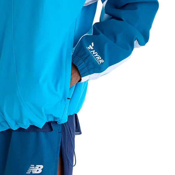 En blå New Balance NYC Marathon-jakke, Herre, Altitude, med hvide indsætninger på ærmerne og New York Road Runners-logoet på manchetten, kombineret med mørkeblå sportsshorts.