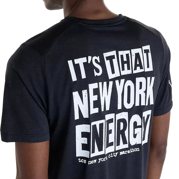 Man ser en person bagfra, iført New Balance NYC Marathon RC Essential Graphic T-shirt til mænd i sort. Den øverste del af ryggen og en del af hovedet er synlige, hvilket fremhæver den hvide tekst på ryggen – »IT’S THAT NEW YORK ENERGY TC5 NEW YORK CITY MARATHON«. Denne ikoniske New Balance-T-shirt er designet til ultimativ komfort med NB ICEx-teknologi og indkapsler ånden i NYC Marathon.