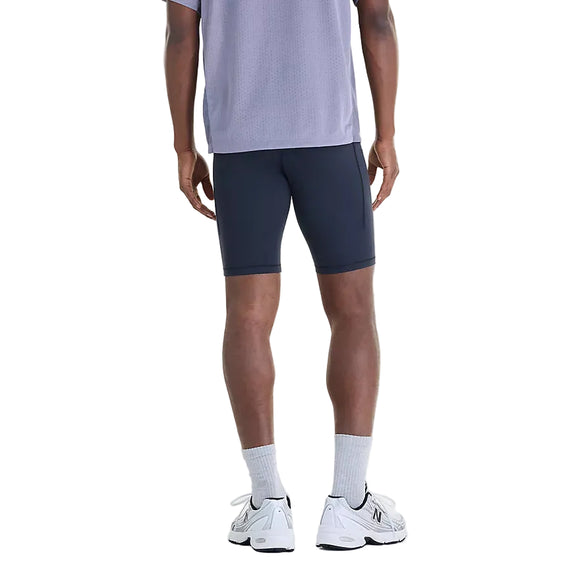 Bagfra-billede af en person iført sorte New Balance NYC Marathon RC Pocket Half Tights 9″, Herre, en grå trøje, hvide sokker og sportssko.