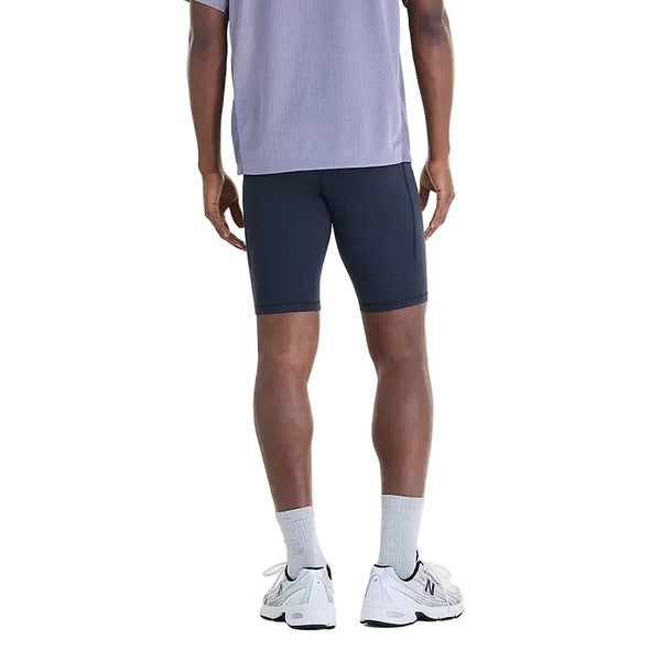 Bagfra-billede af en person iført sorte New Balance NYC Marathon RC Pocket Half Tights 9″, Herre, en grå trøje, hvide sokker og sportssko.