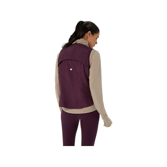 Der ses et billede bagfra af en kvinde med mørkt hår i hestehale, iført en beige langærmet bluse og ASICS Nagino Run Padded Gilet til kvinder i farven Dark Aubergine, kombineret med lilla leggings, mens hun står foran en ensfarvet hvid baggrund.