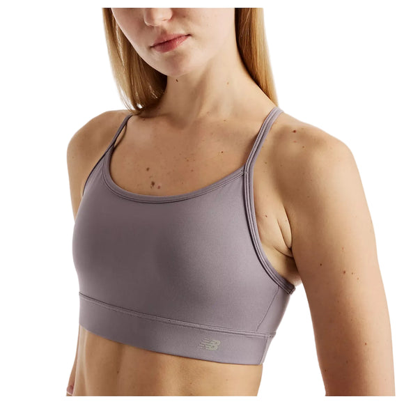 En kvinde med glat, blondt hår har en lyselilla Nb Essential Yoga Bra fra Dame by New Balance på. Den har tynde stropper, en kort pasform ved skuldrene og midten af maven og er forsynet med New Balance-logoet tæt på kanten.