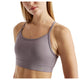 En kvinde med glat, blondt hår har en lyselilla Nb Essential Yoga Bra fra Dame by New Balance på. Den har tynde stropper, en kort pasform ved skuldrene og midten af maven og er forsynet med New Balance-logoet tæt på kanten.